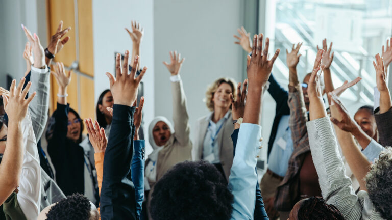 Diverse business group raising hands in unison during a conference, highlighting teamwork, enthusiasm, and collaboration at a professional event